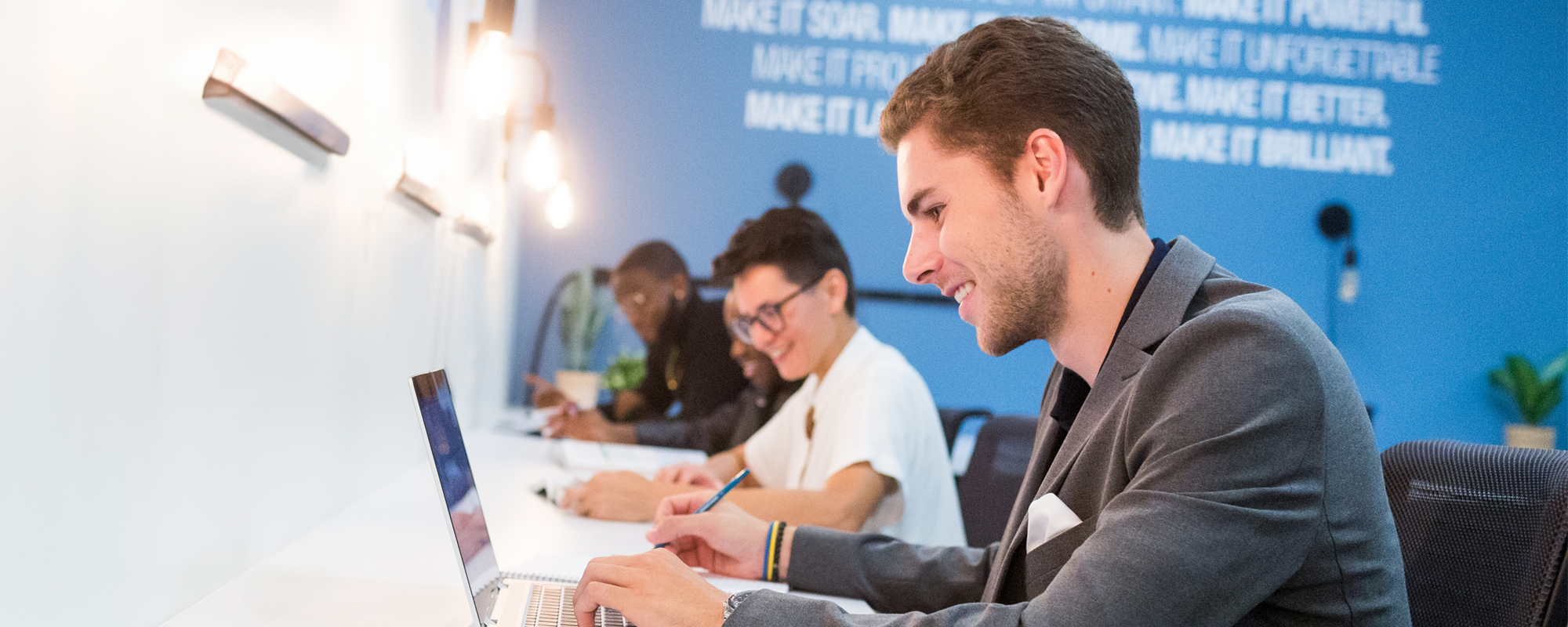 Four students sitting at a counter on laptops.